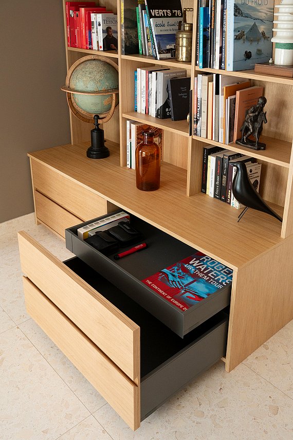 Rangements intégrés d'une bibliothèque sur mesure en placage chêne conçue pour optimiser une pièce de passage.