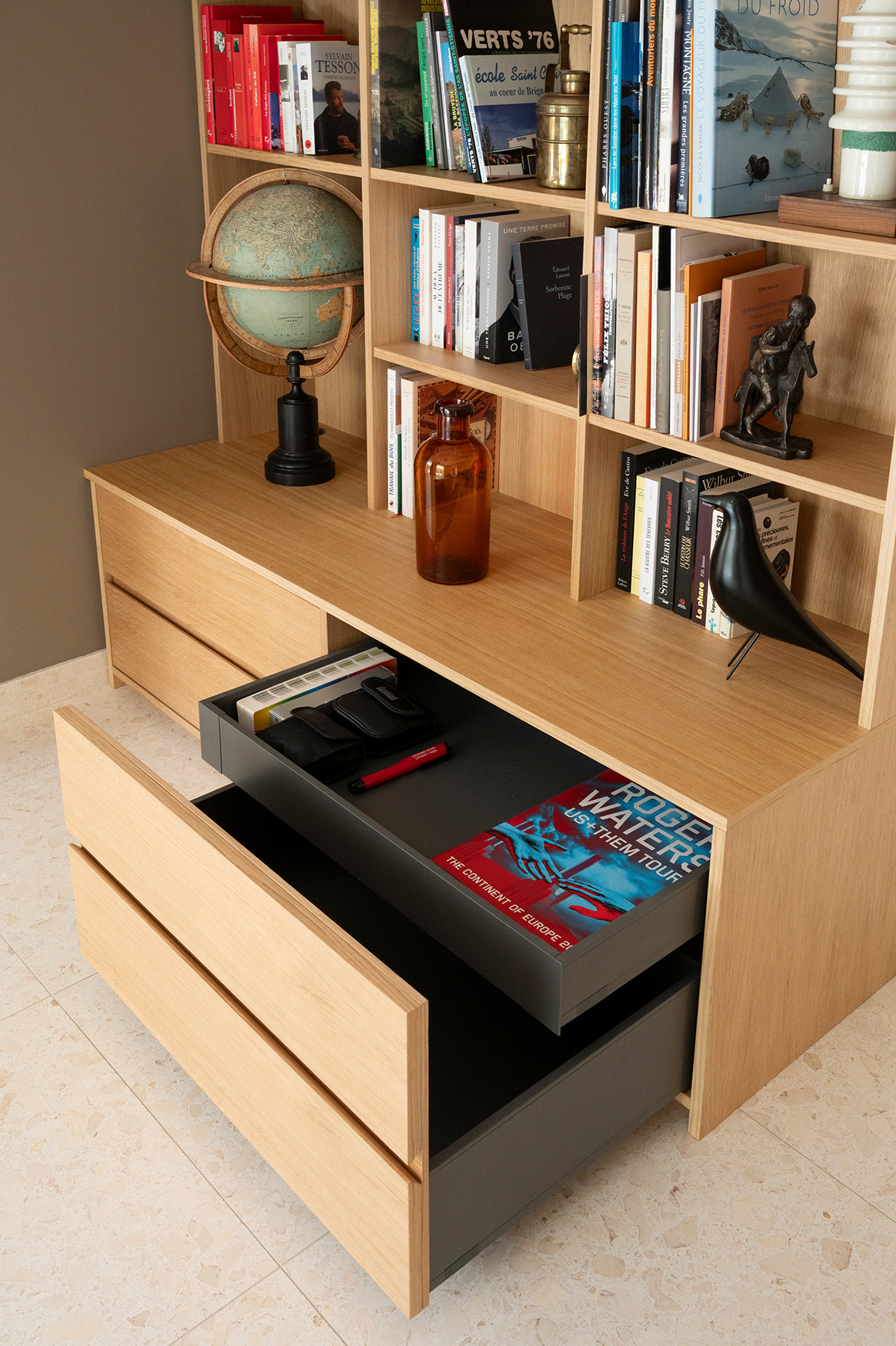 Rangements intégrés d'une bibliothèque sur mesure en placage chêne conçue pour optimiser une pièce de passage.